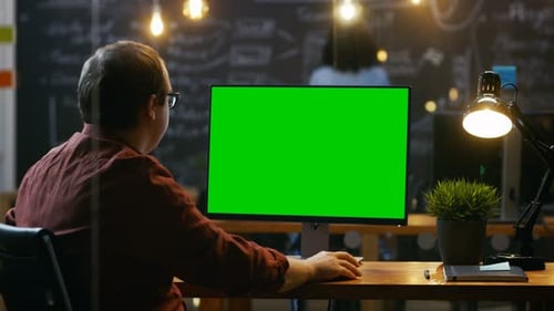 Office Employee at His Desktop Works on a Mock-up Green Screen Personal Computer. Over the Shoulder