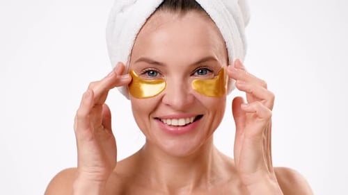 Smiling Woman Applies Golden Eye Patches in Studio