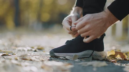 Man Tying Shoelaces of Running Shoe in Park