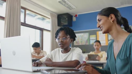 À l'école, un enseignant aide un élève avec un ordinateur portable en classe, d'autres étudient