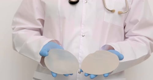 Doctor Holding Up Two Breast Implants in Gloves