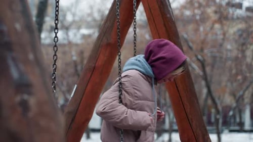 Young Lady Swinging in Snowy Park in Winter Outfit Holding Swing Chains