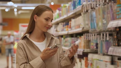A Woman Shopping in a Supermarket The Woman is Standing in the Aisle Looking at a Shelf of Cosmetics