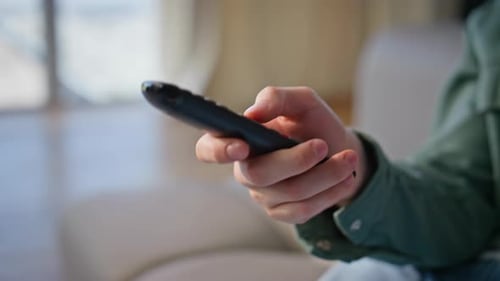 Mann wechselt mit der Hand die Kanäle, Wohnzimmer, Nahaufnahme, Typ, der zu Hause eine TV-Fernbedienung hält