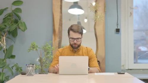Young Businessman Celebrating Online Success on Laptop in Office