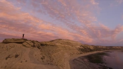 Young Man Silhouette Standing On A Mountain With His Hands Behind The Head Looking To The Sea At Sun