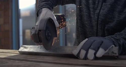 Metalworking in workshop with angle grinder, sparks flying as craftsman in gloves cuts metal