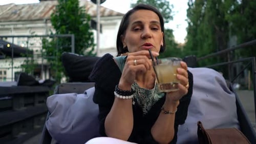 Cheerful woman enjoys cocktail and conversation in a sunny urban cafe
