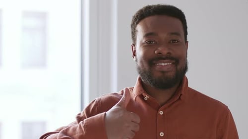 Nahaufnahmeporträt eines jungen Afroamerikaners, der die Daumen nach oben zeigt und in die Kamera lächelt