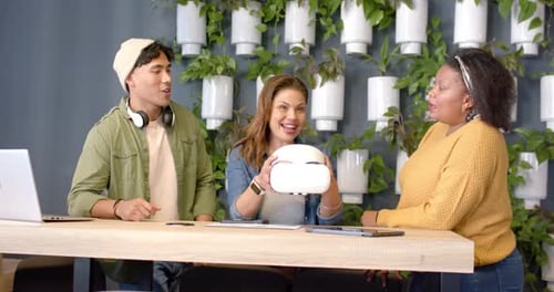 Diverse coworkers grabbing VR headset at office counter testing features and exchanging high-five