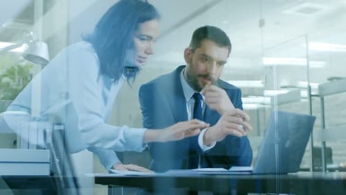 Beautiful Female Manager Consults Handsome Businessman sitting at His Desk. Working on a Laptop in