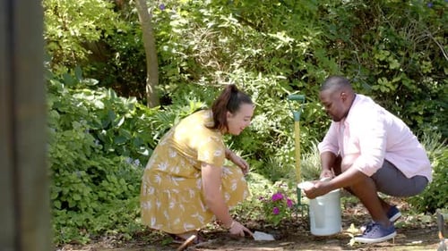 Gardening together, diverse friends planting flowers and watering plants in backyard garden