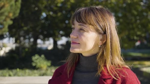 Woman in Red Coat Smiling in City Park