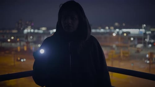 Hooded Figure with Flashlight on Urban Rooftop at Night