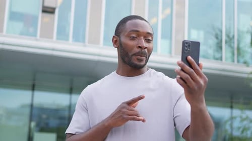 African American Man Holding Smartphone Having Video Chat on Urban Street in City Guy Blogger