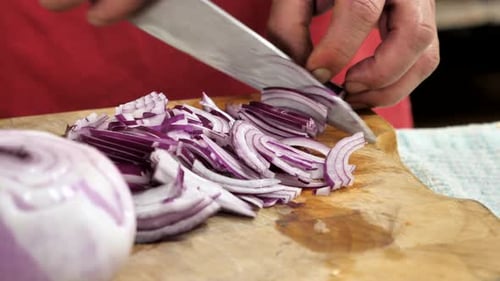 Professional chef prepares and cuts red onion on wood chopping board. Close up and circle pan slow m