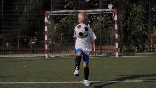 A Little Boy Football Player Trains on the Football Field He Stuffing the Ball