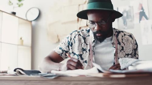 Young Talented Man in Hipsterlike Outfit Sketching a New Fashion Looks in Cozy Fashion Studio