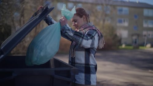 Mujer tirando bolsa de basura en papelera negra