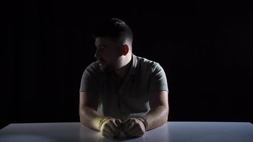 Distressed Man in Handcuffs at Table in Dark Room