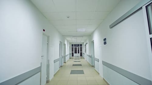 Walking Slowly Down a Corridor Hospital Hall Way with Tiled Floor and Doors Leading Off on Either
