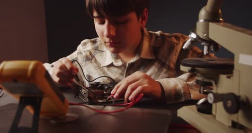 Adolescente concentrado que trabaja con un multímetro y observa las lecturas en el monitor: algo fascinante