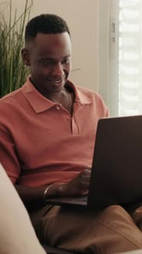 Man Smiles While Using Laptop Indoors During the Day