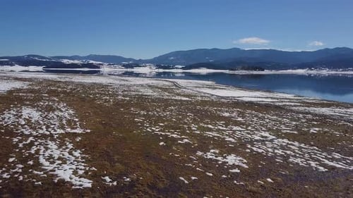 Drone flies over a lake with a reflection of a mountain and sky in winter