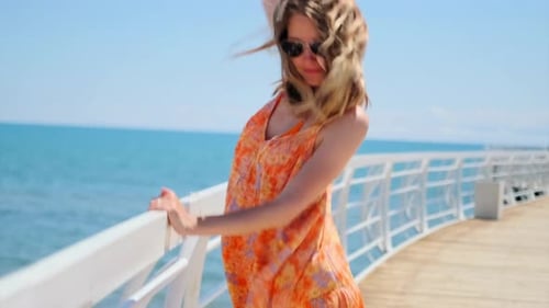 Young woman dancing to music in large headphones on pier against backdrop of blue sky