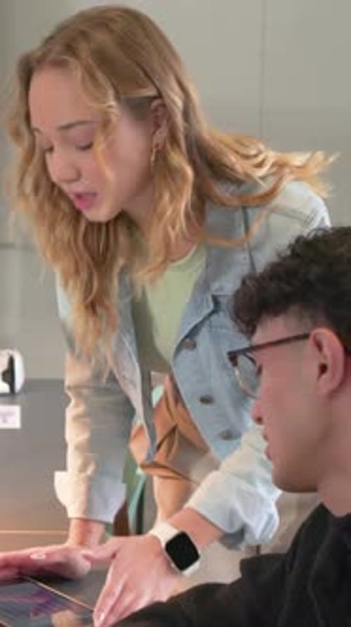 Woman leaning over tablet and tapping, guiding colleague in education lounge, walking toward sofa