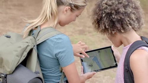 Junge kaukasische Frau und biraziale Frau untersuchen ein Tablet im Freien