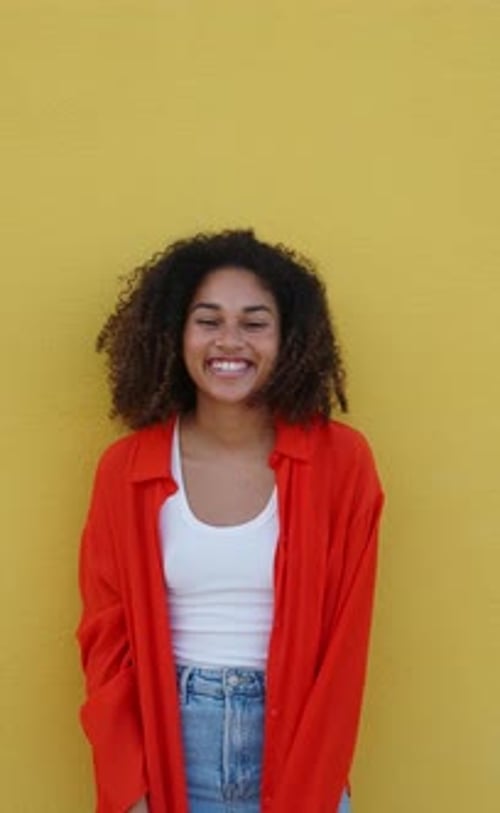 Vertical Video Portrait of a Smiling Happy African American Girl Looking at Camera on a Yellow Wall