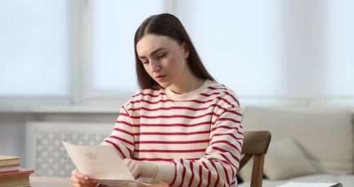 Upset woman reading letter from university at table indoors