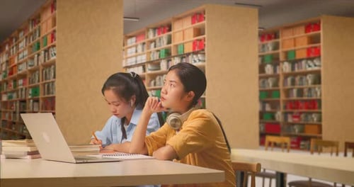 Student Thinking While Sitting With Her Classmate Writing Into The Notebook In The Library