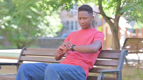 Young Adult Waiting on Bench Checking Smartwatch