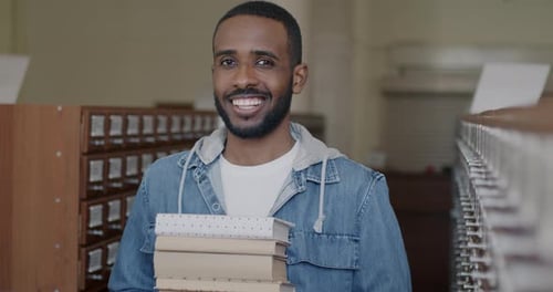 Smart African American Student Standing in University Library Holding Books Smiling Looking at