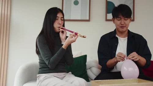 Young adults blowing up balloons at home on couch