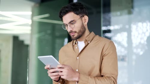 Handsome businessman is using digital tablet while standing in business office. Manager works