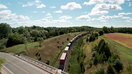 Un tren de carga infinito recorre un paisaje de valle cubierto de hierba debajo del puente mientras el automóvil pasa por la carretera
