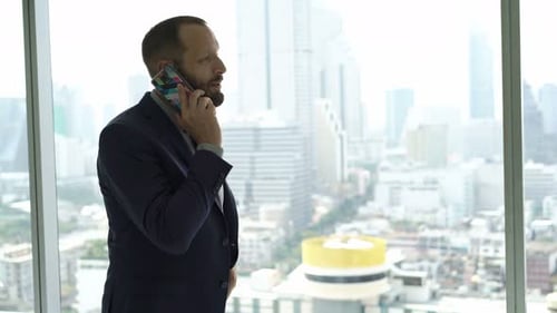Young Businessman Talking on Cellphone and Admire View From Window in Office 30s