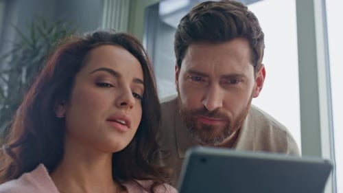 Interested Spouses Watching Tablet Computer Talking Together at Kitchen Closeup