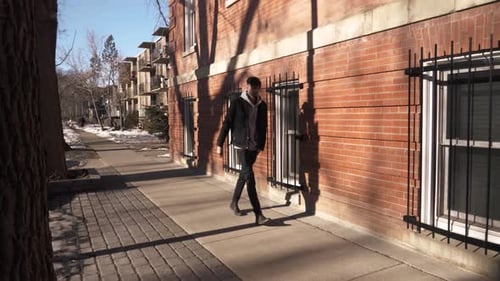 Young man walks on sunny urban sidewalk outside a brick building