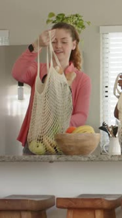 Vídeo vertical: La llegada de la bolsa hace que una mujer con una chaqueta rosa levante una bolsa de malla en el mostrador clasificando la fruta
