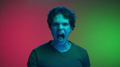Portrait of Young Man Looking at Camera and Screaming in Neon Lighting of Studio
