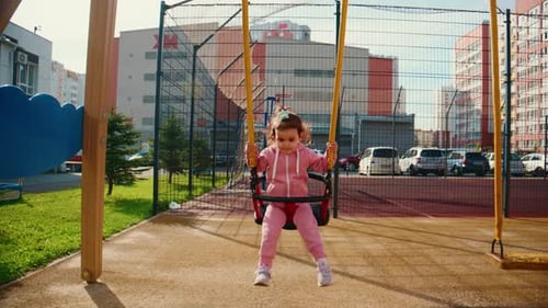 Ein fröhliches Kind in einem rosafarbenen Outfit schaukelt glücklich auf dem Spielplatz und zeigt einen Moment voller Verspieltheit