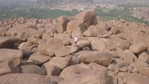 Aerial follows lone male tourist in mountain of granite rock boulders