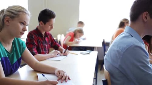 Young students writing a test together in school notebooks and smiling