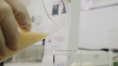 Woman Pours Milk Into Beaker with Measuring Scale on Table