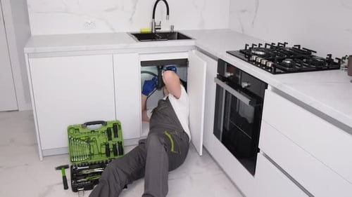 Сантехник чинит раковину для мытья посуды Профессиональные сантехнические услуги