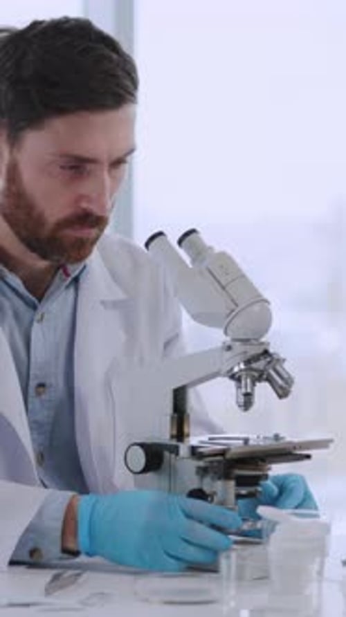Bearded Scientist Using Microscope in Bright Laboratory